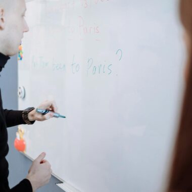 Teacher explaining English lesson using a whiteboard in a classroom setting.
