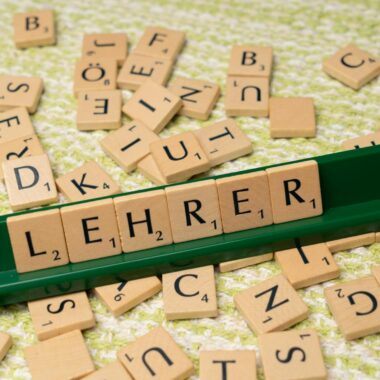Wooden letter tiles spelling 'Lehrer' on a green rack, surrounded by scattered tiles.